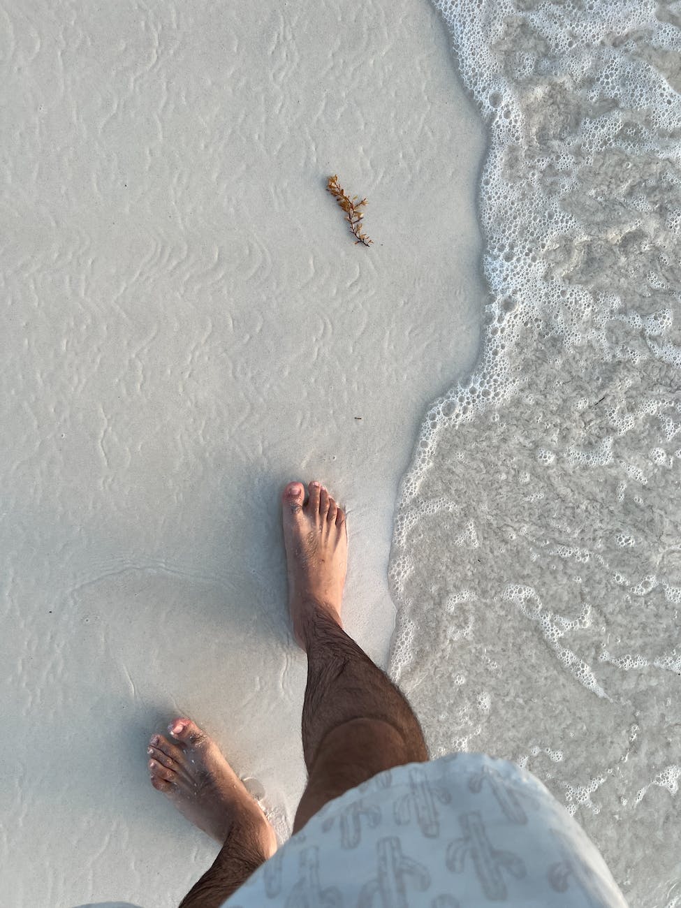 top view of a man standing barefoot on a sandy beach with sea foam